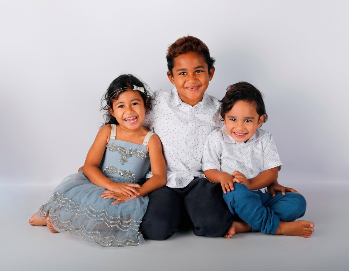 Three siblings smiling together in a family portrait